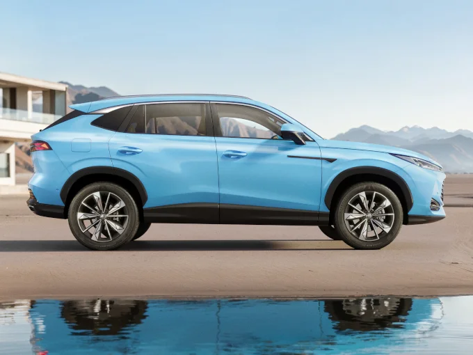 Light blue MG SUV parked by the water with mountains in the background